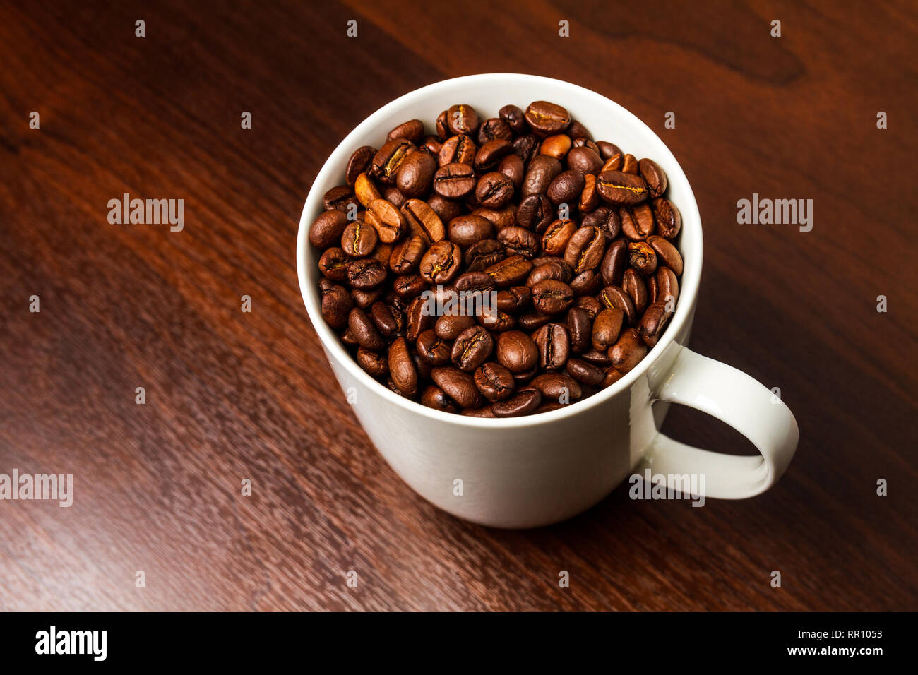 Roasted Coffee beans in a white mug cup isolated on a rustic wood table ...