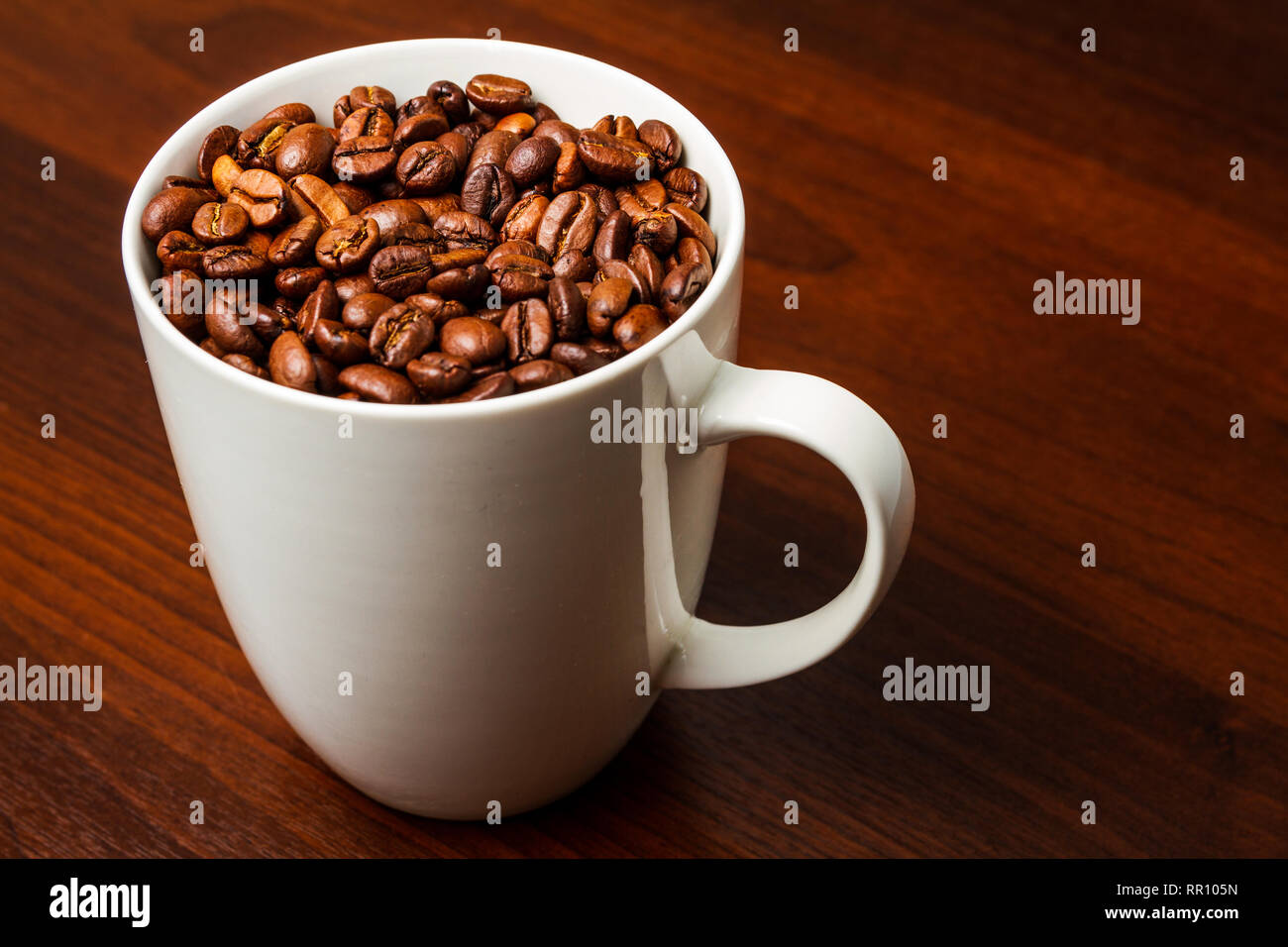 Roasted Coffee beans in a white mug cup isolated on a rustic wood table ...