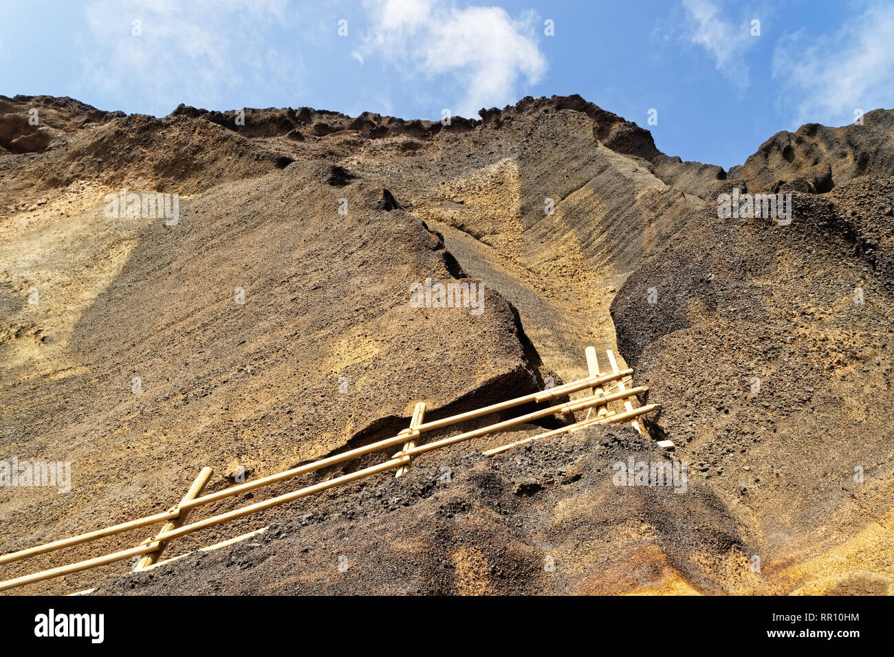 View from below on a steep cliff face in yellow tones, through which leads a climbing path attached with a wooden railing, traces of erosion, over it  Stock Photo