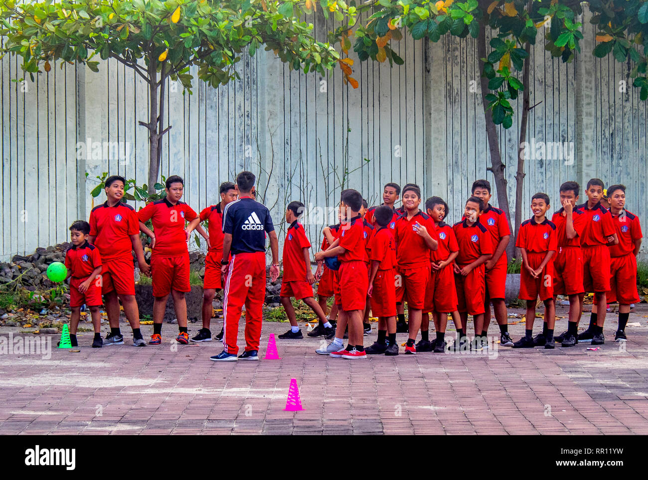 Schoolchildren in red sports uniform  their teacher playing a ball game in Jimbaran Bay Bali Indonesia. Stock Photo