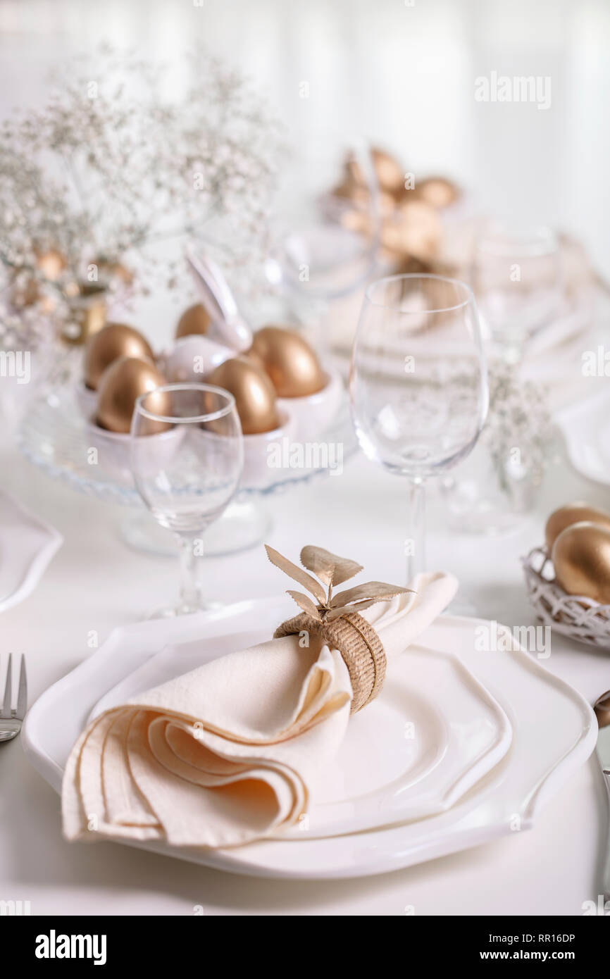 Happy Easter! Golden decor and table setting of the Easter table with white dishes of white color. Selective focus. Stock Photo