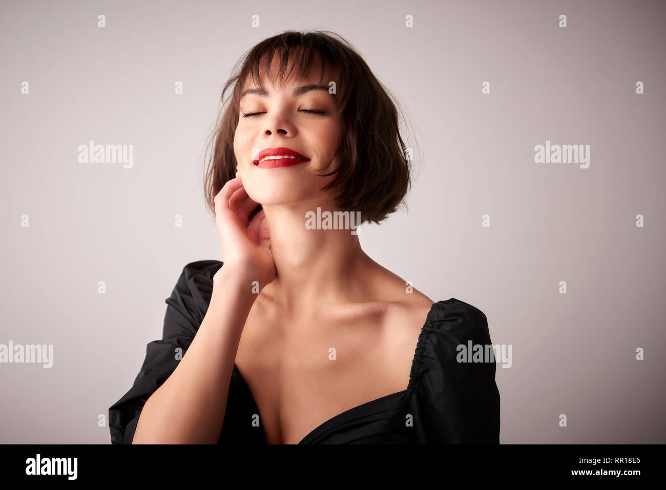 Studio portrait of smiling young woman with closed eyes posing at light ...