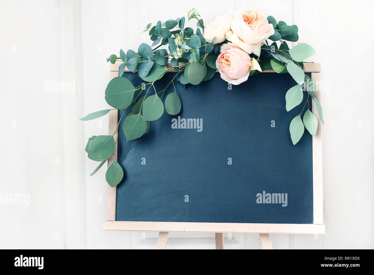 Blank wedding chalkboard sign mockup scene. Floral garland of green eucalyptus branches and apricot English roses flowers. Rustic birthday party Stock Photo