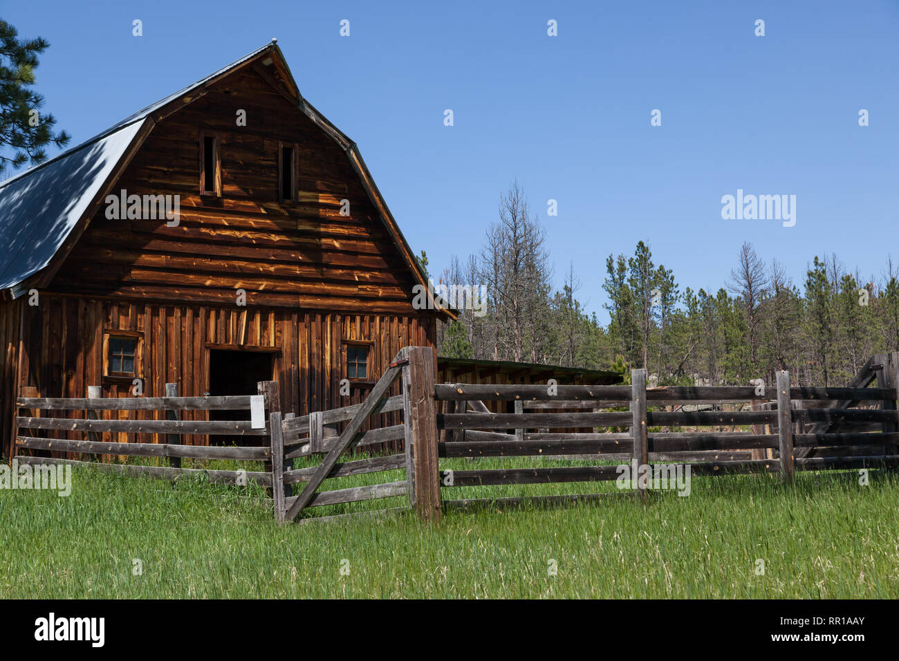 An old wooden barn with a fenced in corral and tall green grass on an