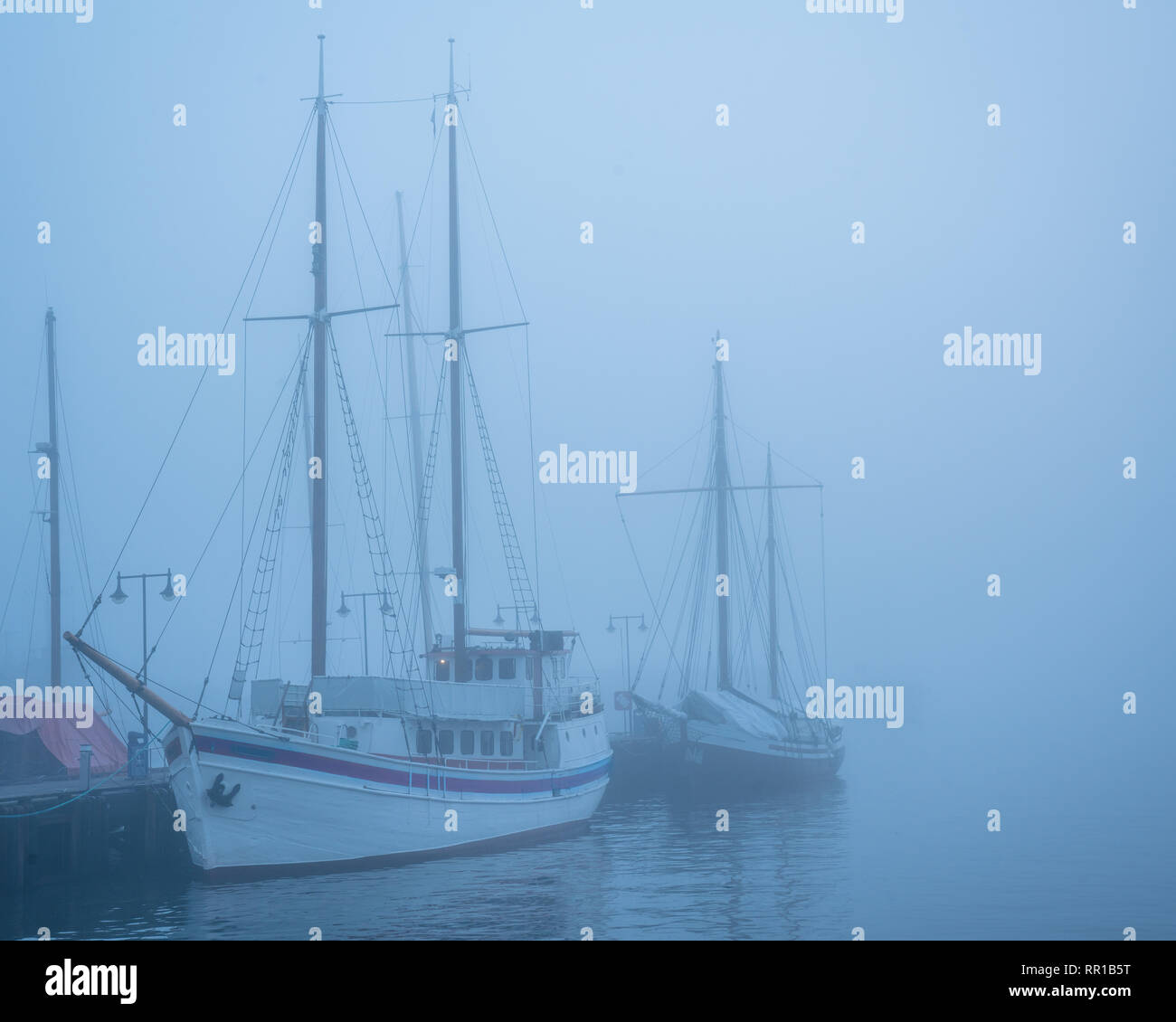 Misty romantic sail boats without sails in the water near a dock Stock Photo
