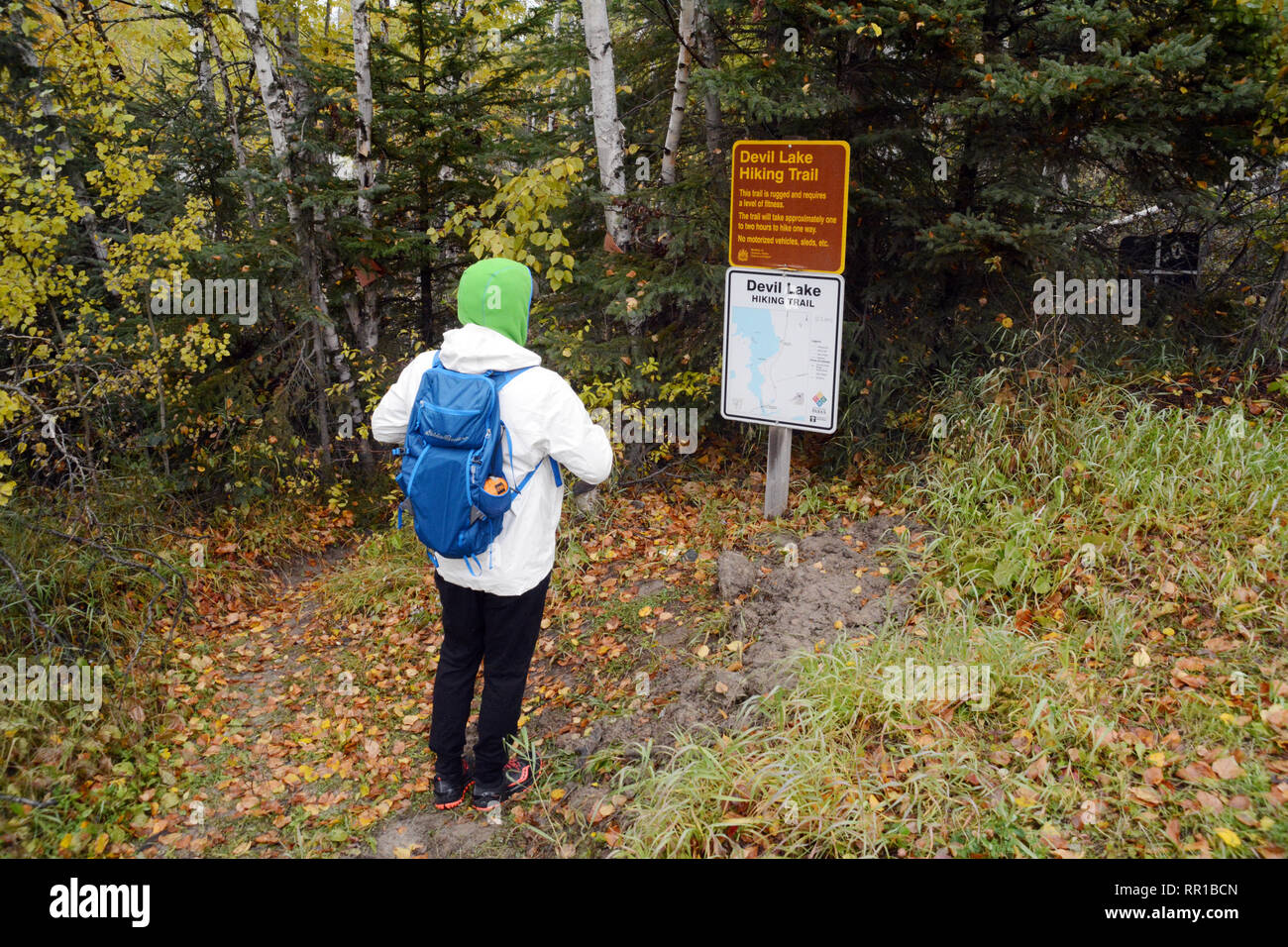 A male hiker with a daypack reads the sign at the trailhead of the Devil Lake hiking trail, near Stanley Mission, in northern Saskatchewan, Canada. Stock Photo