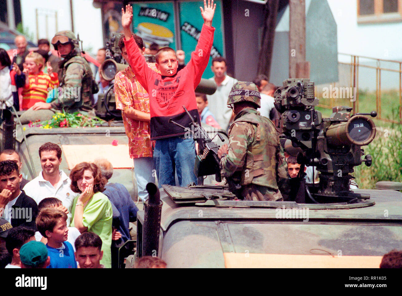 1999 - Ethenic Albanians gather in the streets for a parade held to honor American Forces in the Kosovo village of Koretin.  Kids climb on top of an M998 High-Mobility Multipurpose Wheeled Vehicle (HMMWV) with TOW missile. Stock Photo