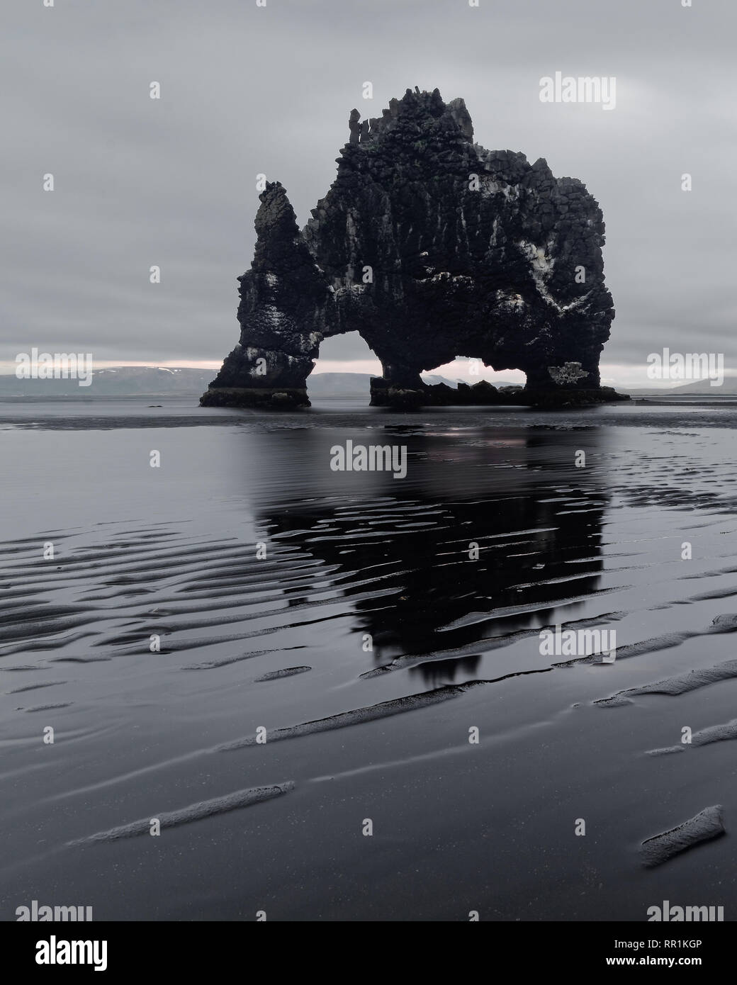 Scenic view of a striking rock formation in shallow water on a black beach with a pattern of sandstrips - Location: Iceland, east coast of the Vatnsne Stock Photo