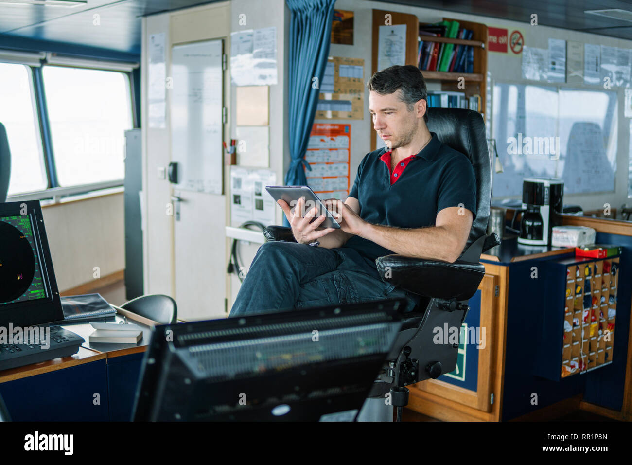 chief officer on navigation bridge watching digital tablet. Stock Photo