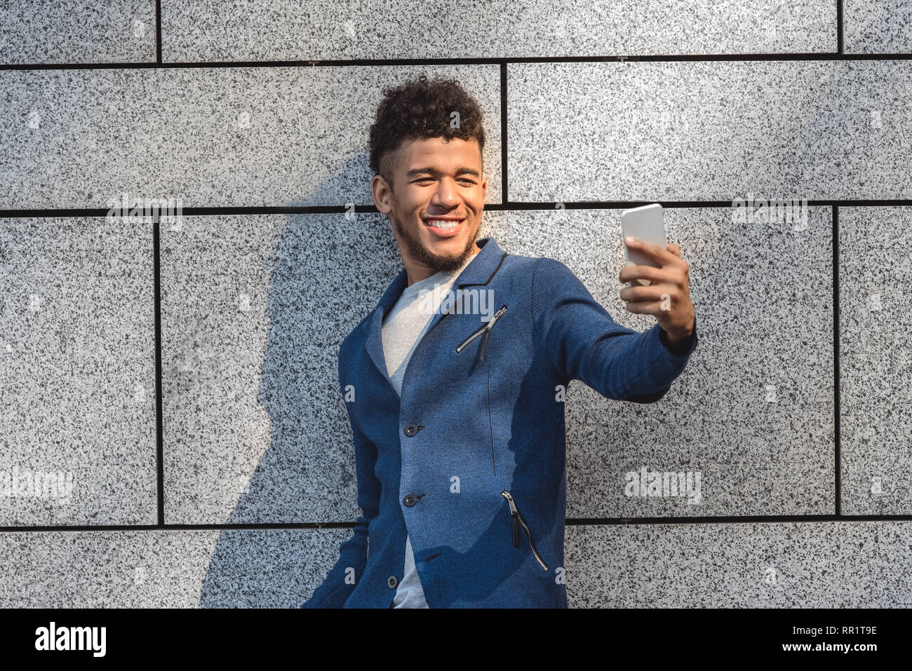 Freestyle. Mulatto guy standing isolated on wall taking selfie on smartphone cheerful Stock Photo
