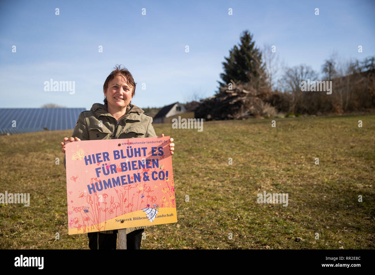 23 February 2019, Bavaria, Heilbronn: Isabelle Hirsch, conventional farmer and supporter of the petition for a referendum 'Biodiversity' is standing on one of her meadows with a sign with the inscription 'Hier blüht es für Bienen Hummeln und Co! The 52-year-old and her husband have given away all the animals, built photovoltaic collectors on the barn roofs and since then have only cultivated grassland. The sale of hay and silage accounts for about one third of the turnover, with a further third coming from electricity generation and the rental of holiday homes. (to dpa-Korr: 'Bio alone is not Stock Photo