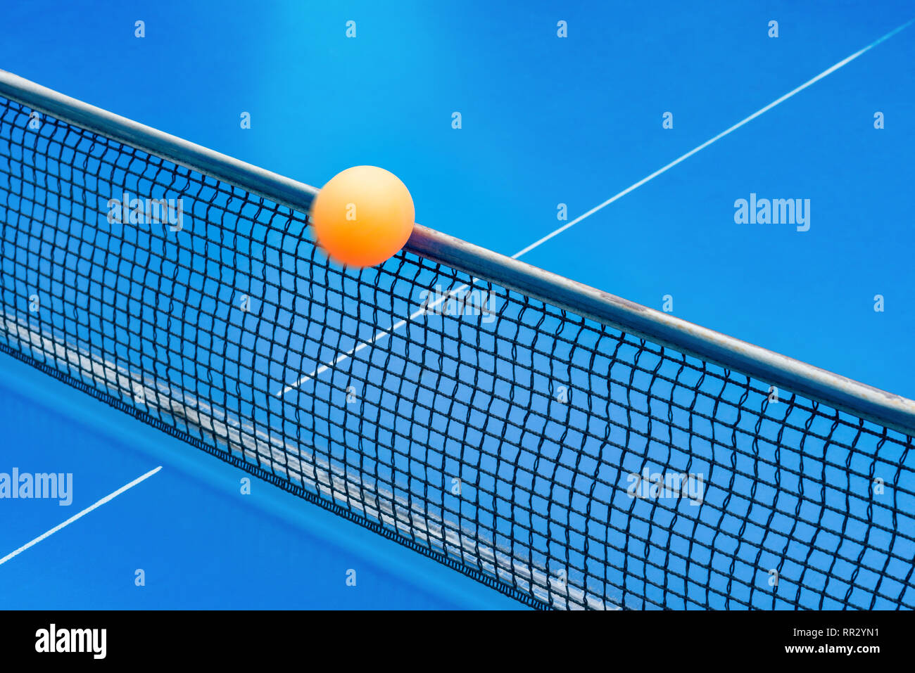 yellow ball hits the netting on a blue pingpong table Stock Photo