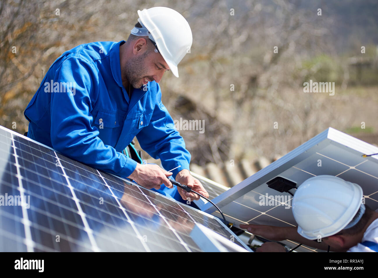 Male engineers installing solar photovoltaic panel system. Electricians mounting blue solar module on roof of modern house. Alternative energy resources concept. Stock Photo