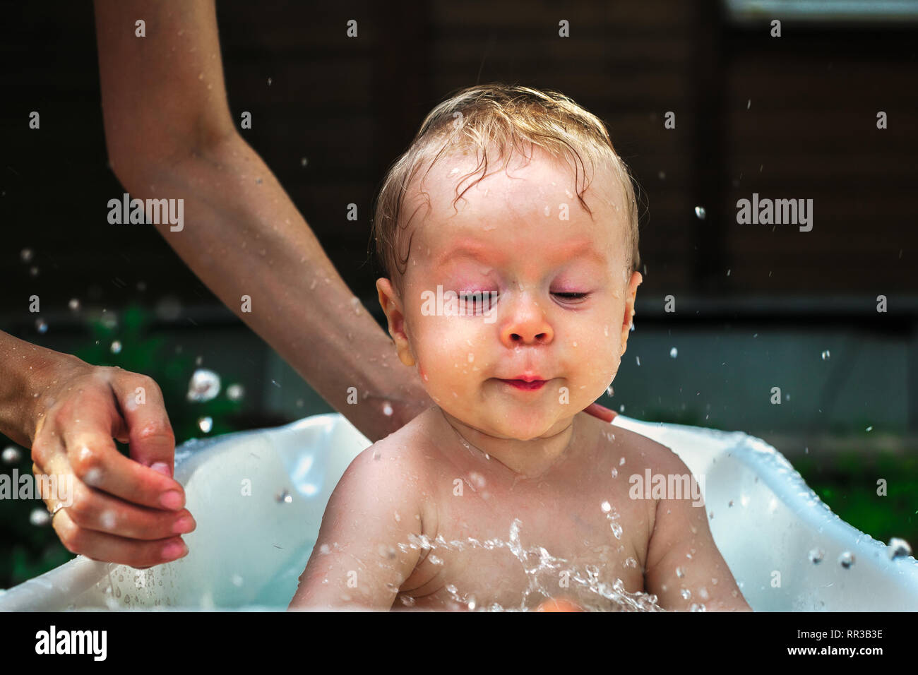 Child in harmony with nature playing fun with water and taking bath outdoors on the grass in bowl in the village Stock Photo