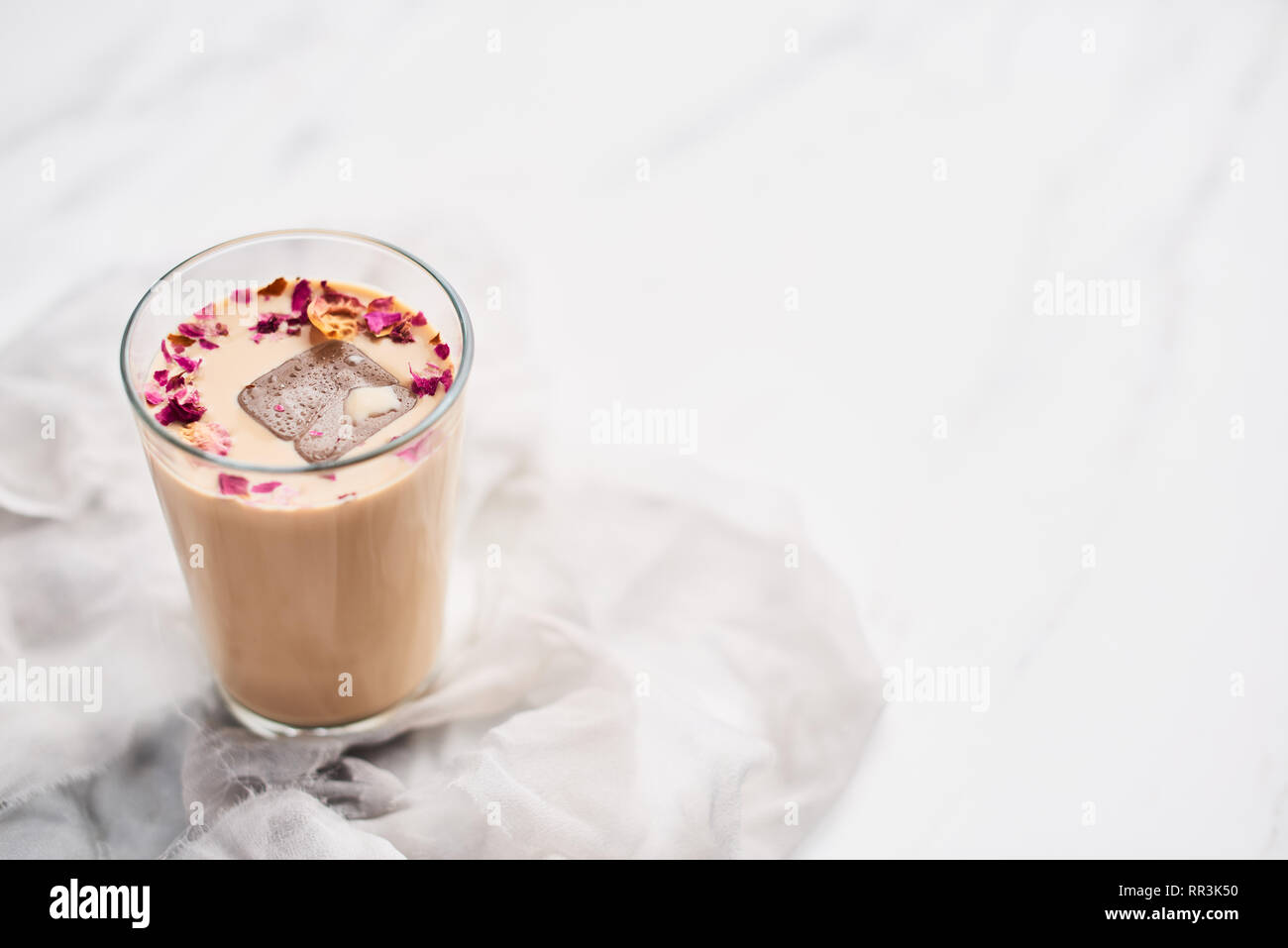 Iced coffee with rose and cardamom in a tall glass on white and gray silk background. Copy space for text. Stock Photo