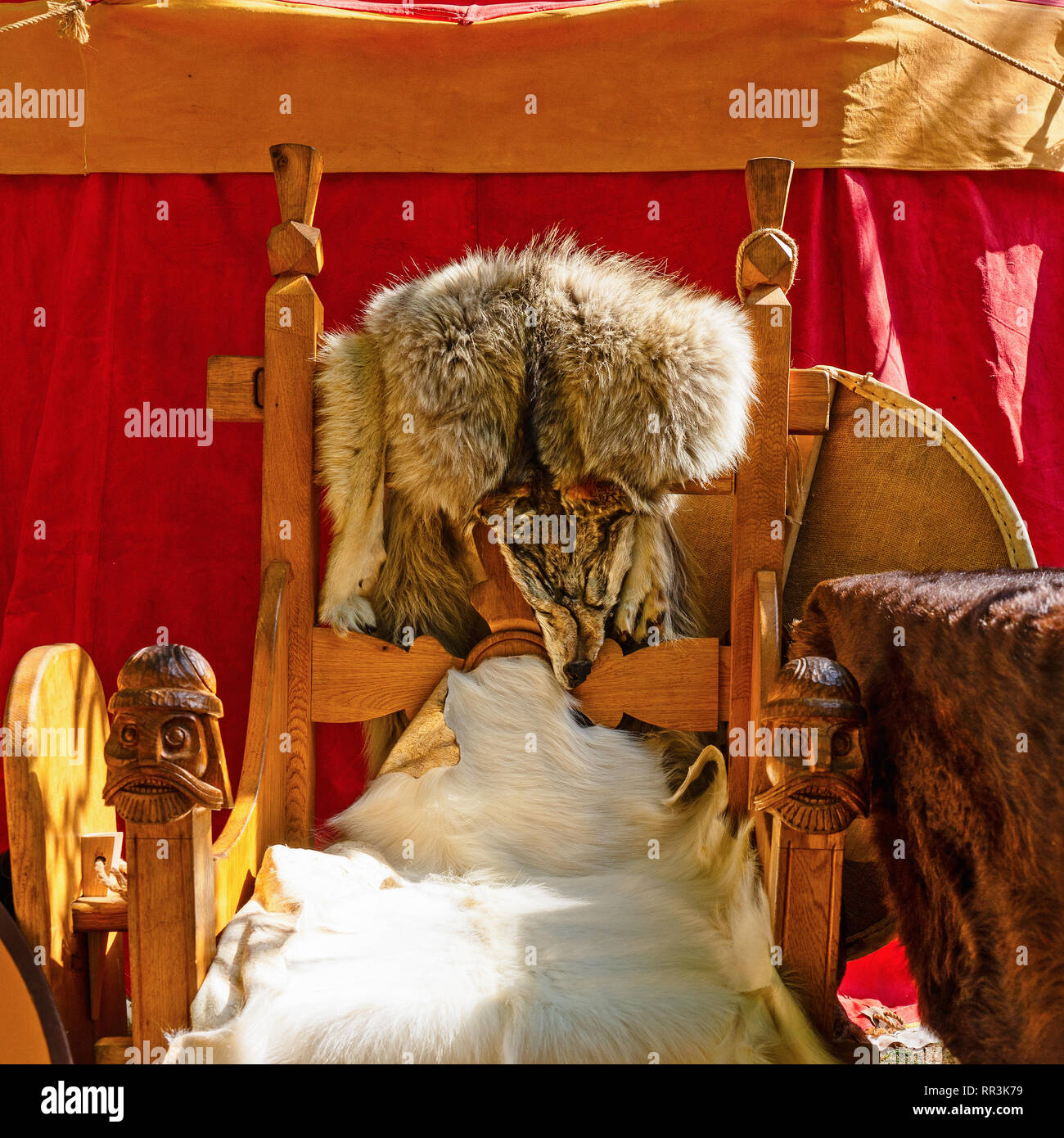 Barbarian, Norseman, Viking king or Koenig chair, seat or throne covered with a wolf, goat furs or skins stand in a sunny spot by the red pavilion Stock Photo