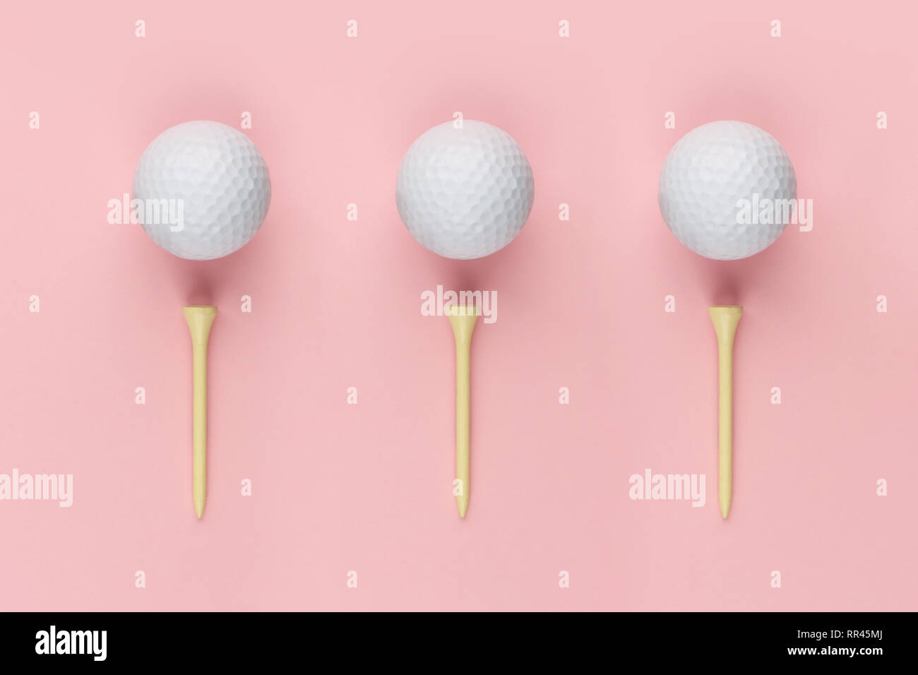 Three golf ball and wooden tee on pink background closeup Stock Photo