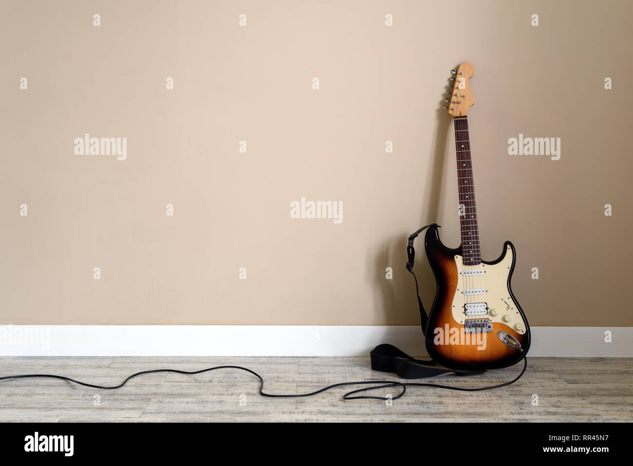 Electro guitar with cable on wall background. Music instrument concept Stock Photo