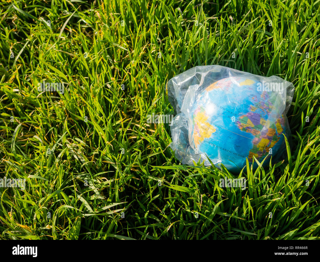 A terrestrial globe or planet Earth lying on the grass inside a plastic bag. Concept of ecology Stock Photo