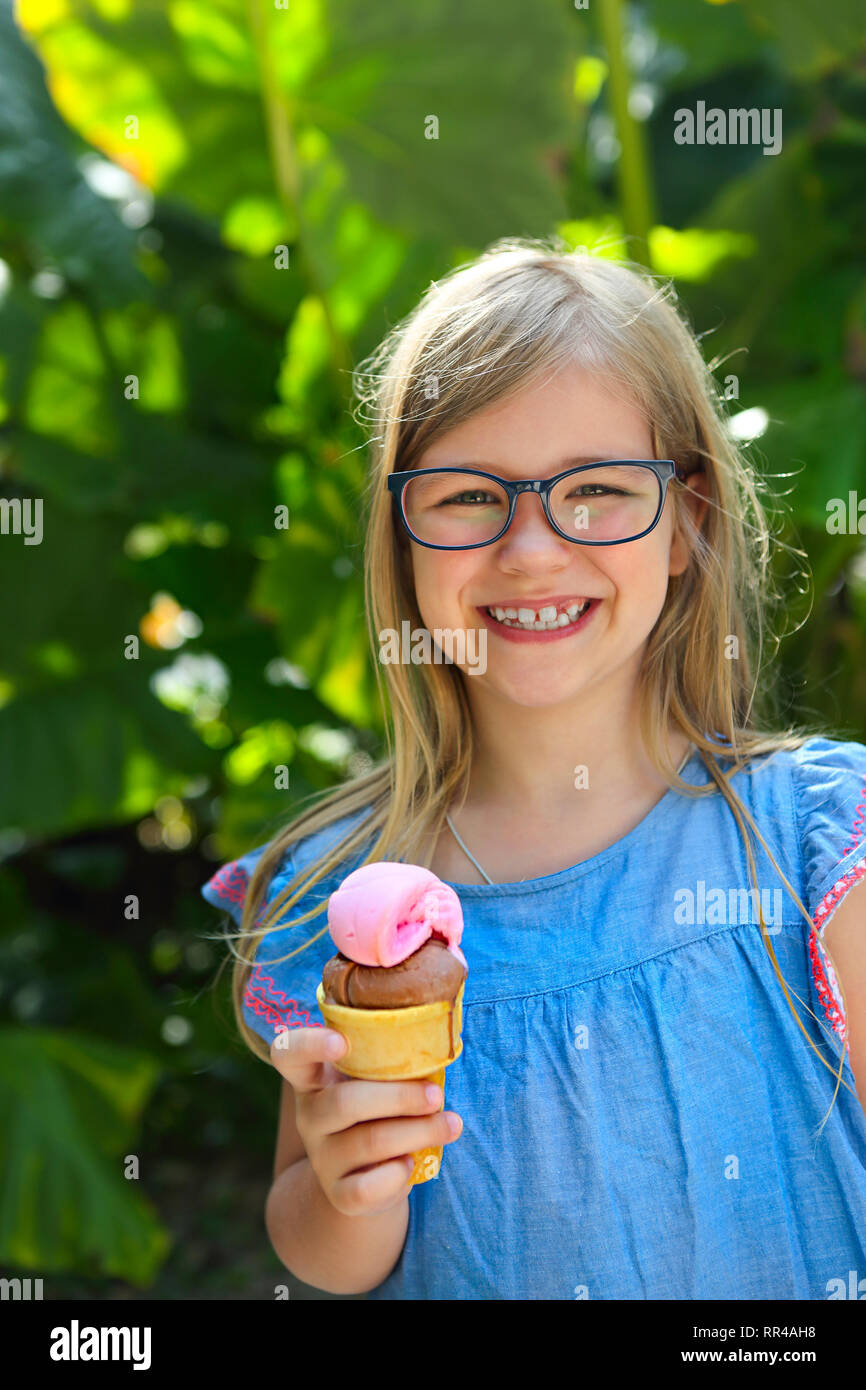 Portrait of the cute little girl with funny expression holding ice cream cone outside against bright nature background Stock Photo