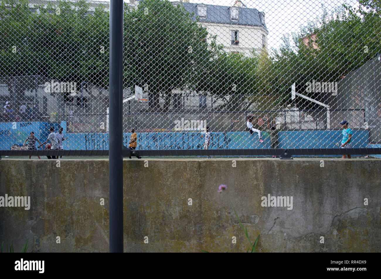 Children and teenagers play and hang-out in fenced football pitch, Square Léon, Rue des Gardes, Goutte d'Or, 75018, Paris, France Stock Photo