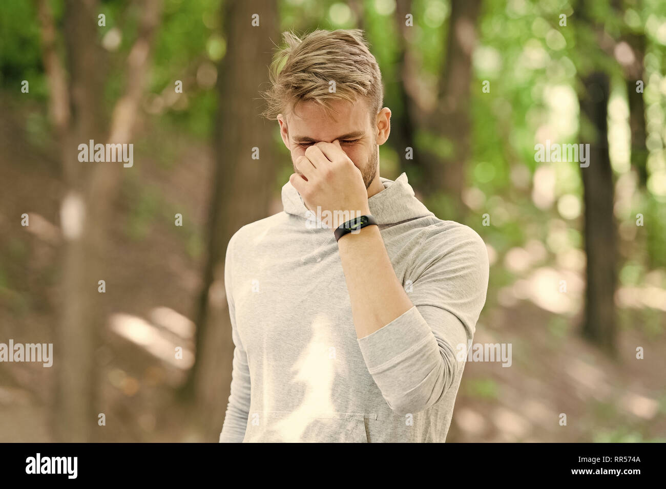 Pain after workout. Man jogger stop running in park because of headache or  nose bleeding. Runner with pedometer band finished training because of  pain. Man runner workout outdoor feel pain Stock Photo -