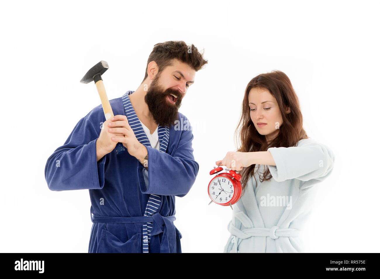 Lets get rid of this annoying alarm clock. Couple in bathrobes going to destroy alarm clock and stay at home. Breaking rules. Tired of early awakening. Man with hammer beat alarm clock. Hateful sound. Stock Photo