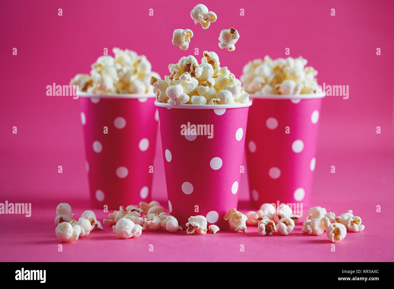 Tasty popcorn falling into cups on pink background. Salty fresh crusty