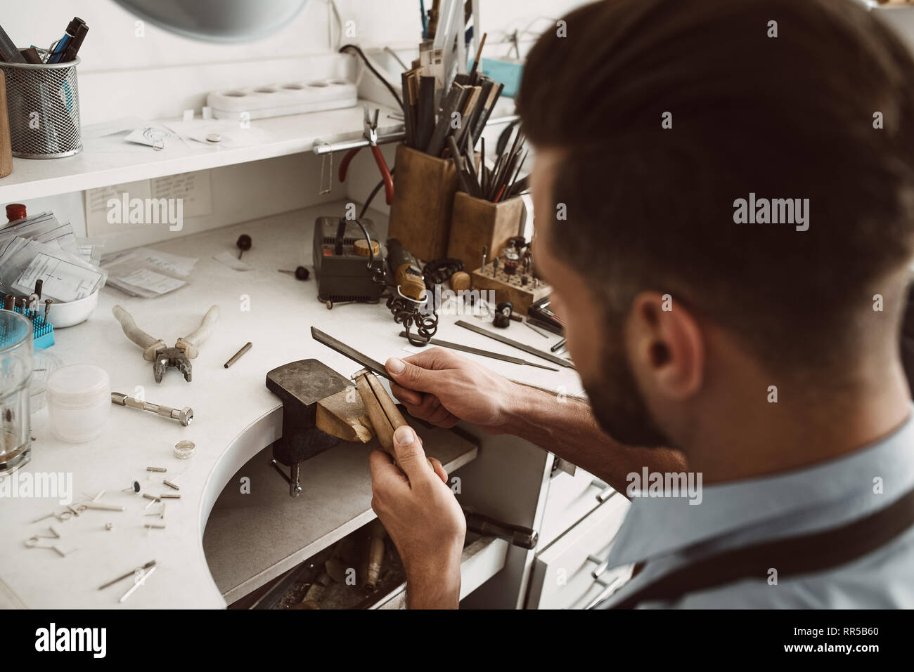 Handmade. Back view of young male jeweler making a ring at his workbench. Jewelry making process. Jewelry equipment. Working process. Jewelry manufact Stock Photo