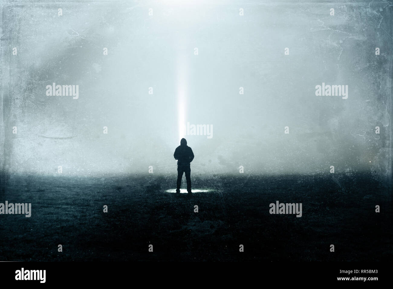 An eerie silhouette of a lone hooded figure in a field with a torch. With a dark, spooky blurred abstract, grunge effect edit. Stock Photo