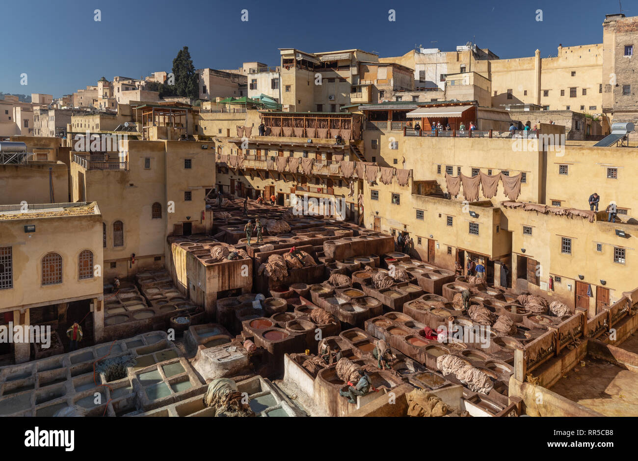 Workers at the dye vats with tourists observing from balconies above, Chouara Tannery, Fes, Morocco Stock Photo