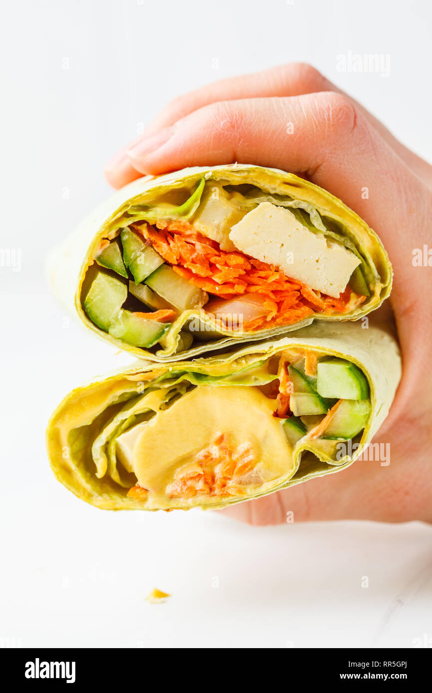 Vegan tofu wraps with cashew cheese sauce and vegetables in hand, white background. Plant based food concept. Stock Photo