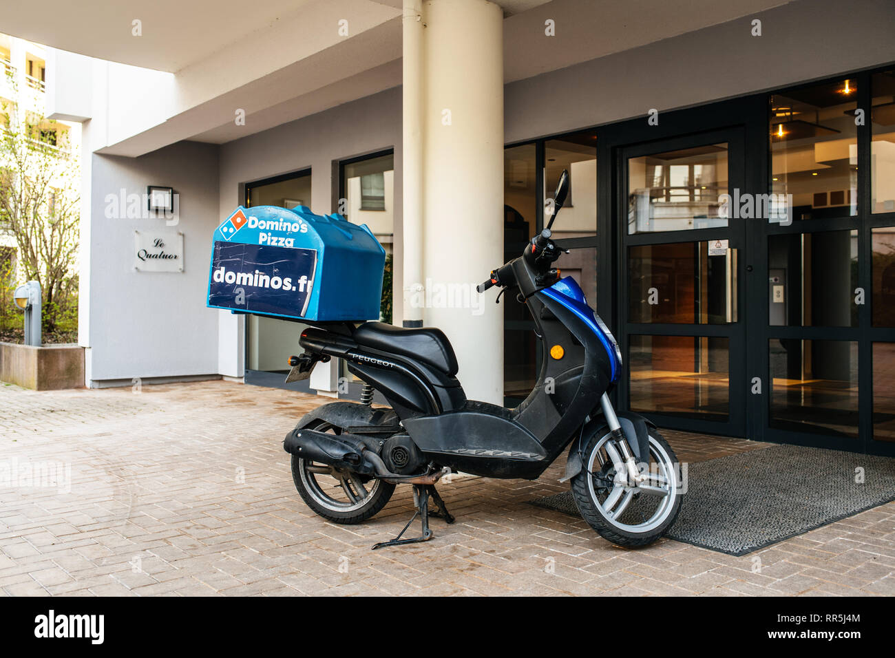 Strasbourg, France - Apr 8, 2018: Pizza delivery scooter parked in front of the apartment building entrance with large DOMINO inscription on the storage compartment Stock Photo
