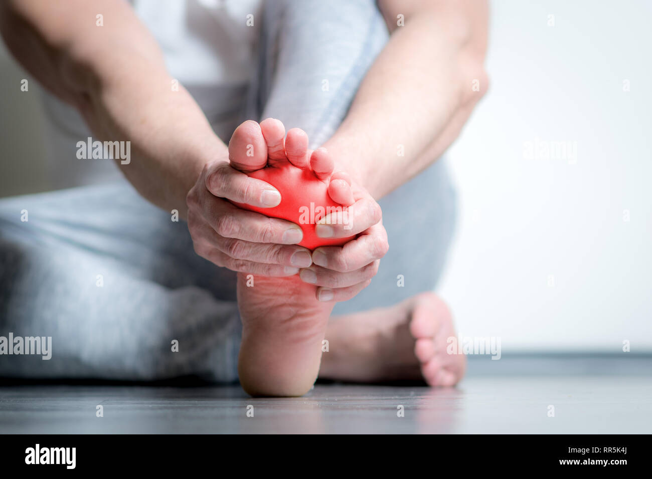 Causian man holds hands to his painful feet, pain in foot, red color is