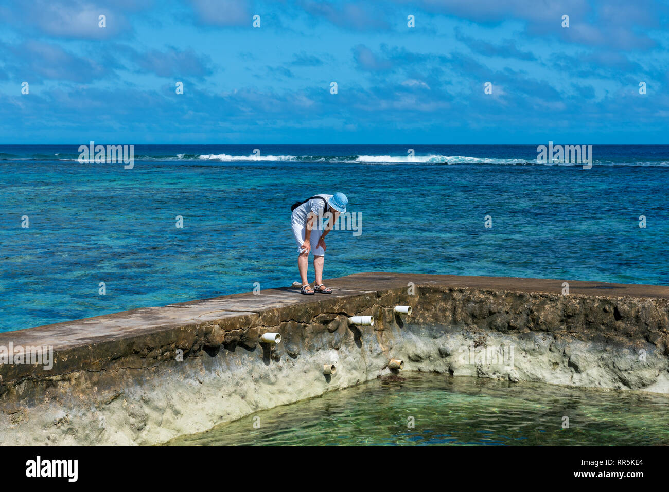 Nuku'Alofa, Tonga -- March 10, 2018. A tourist stands on a short wall and inspects an ocean pool in Tonga. Stock Photo