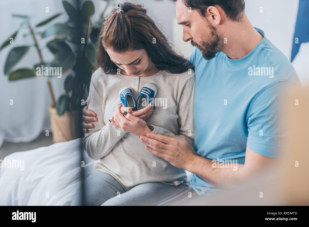 selective focus of sad husband hugging grieving wife with baby shoes Stock Photo
