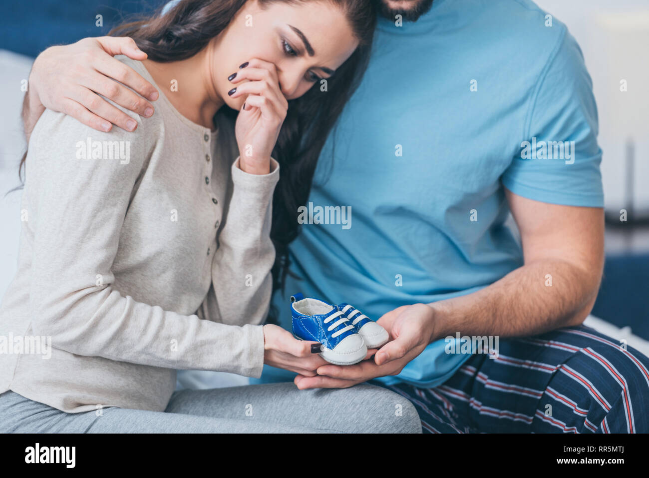 selective focus of husband hugging grieving and crying wife with baby shoes Stock Photo
