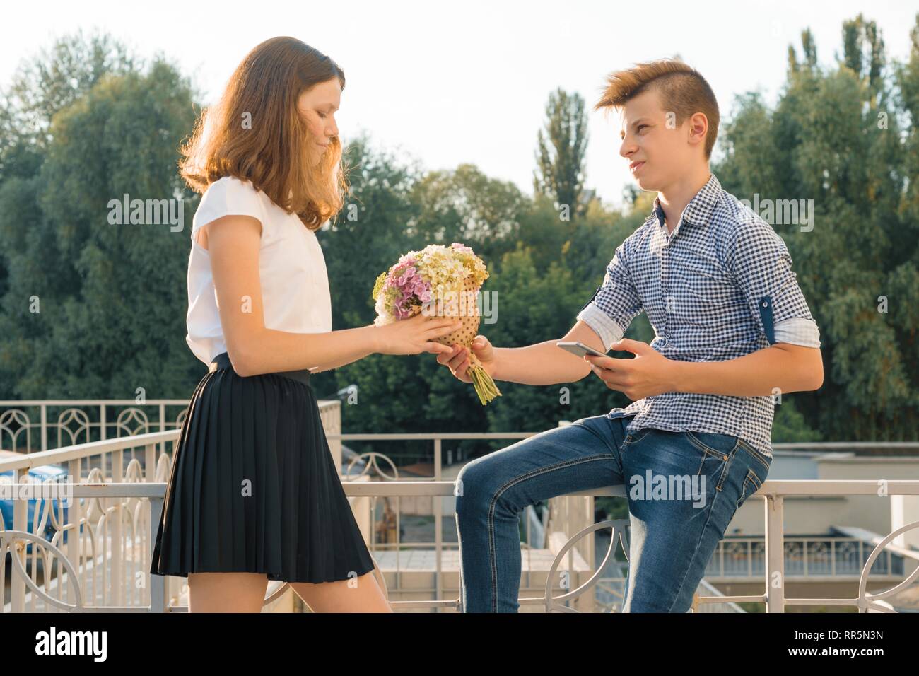 Boy gives girl bouquet of flowers. Outdoor portrait of couple teenagers