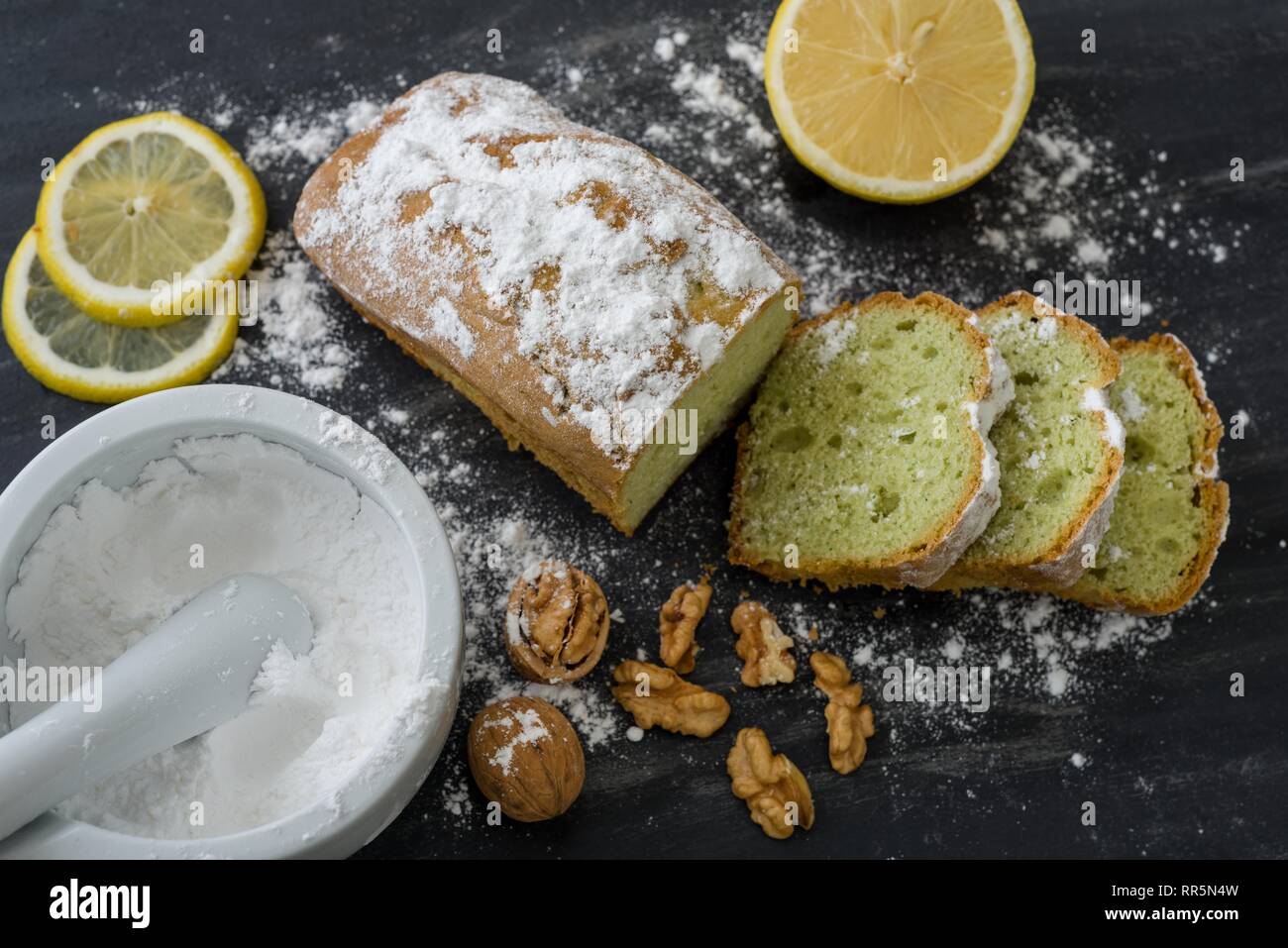 Mint cake on black surface with lemon, nuts, powdered sugar. Stock Photo