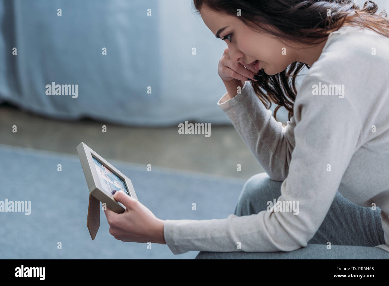 selective focus of upset woman looking at picture frame, crying and ...