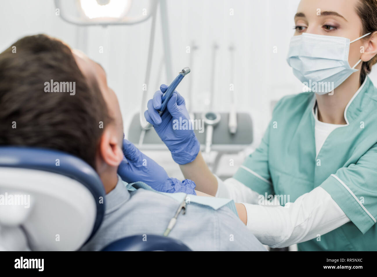 female dentist in mask holding dental instrument while touching face of