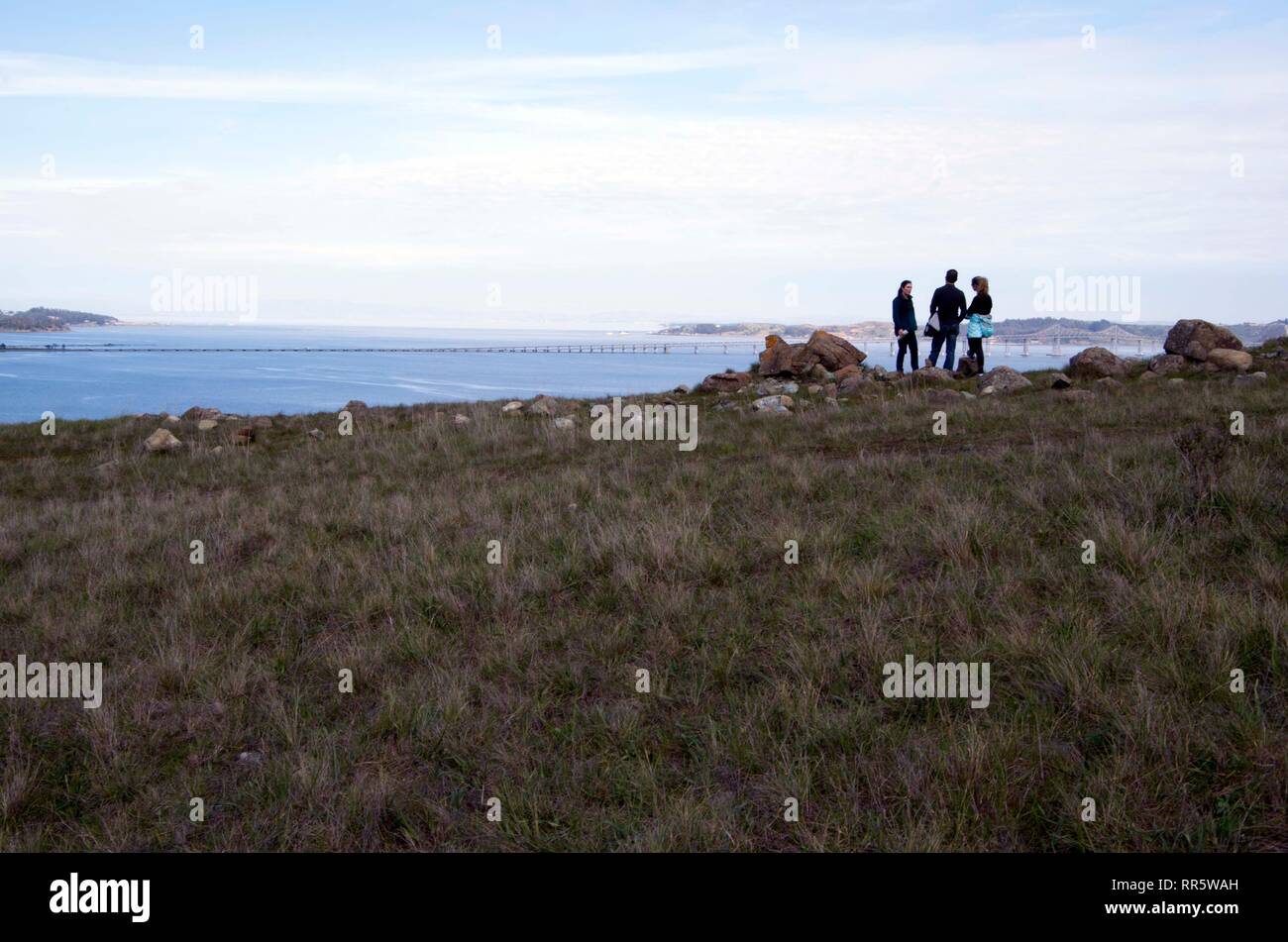 Three people take a break on the way to the top of Ring Mountain in Marin County. They stopped to appreciate the view of the Richmond Bridge. Stock Photo