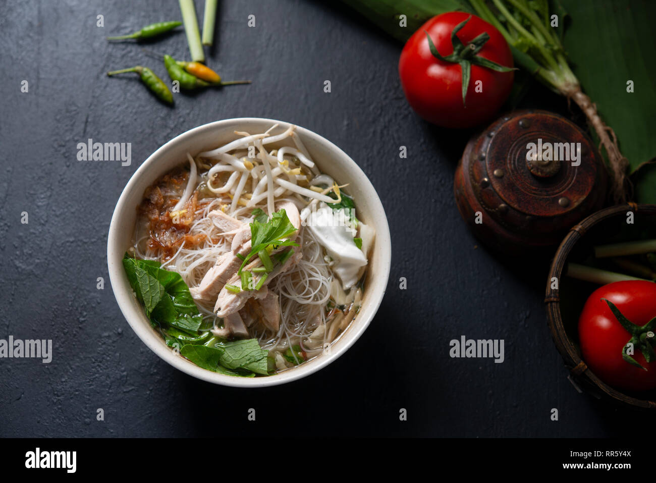 Asian rice noodles soup and chicken in bowl on dark background. Top