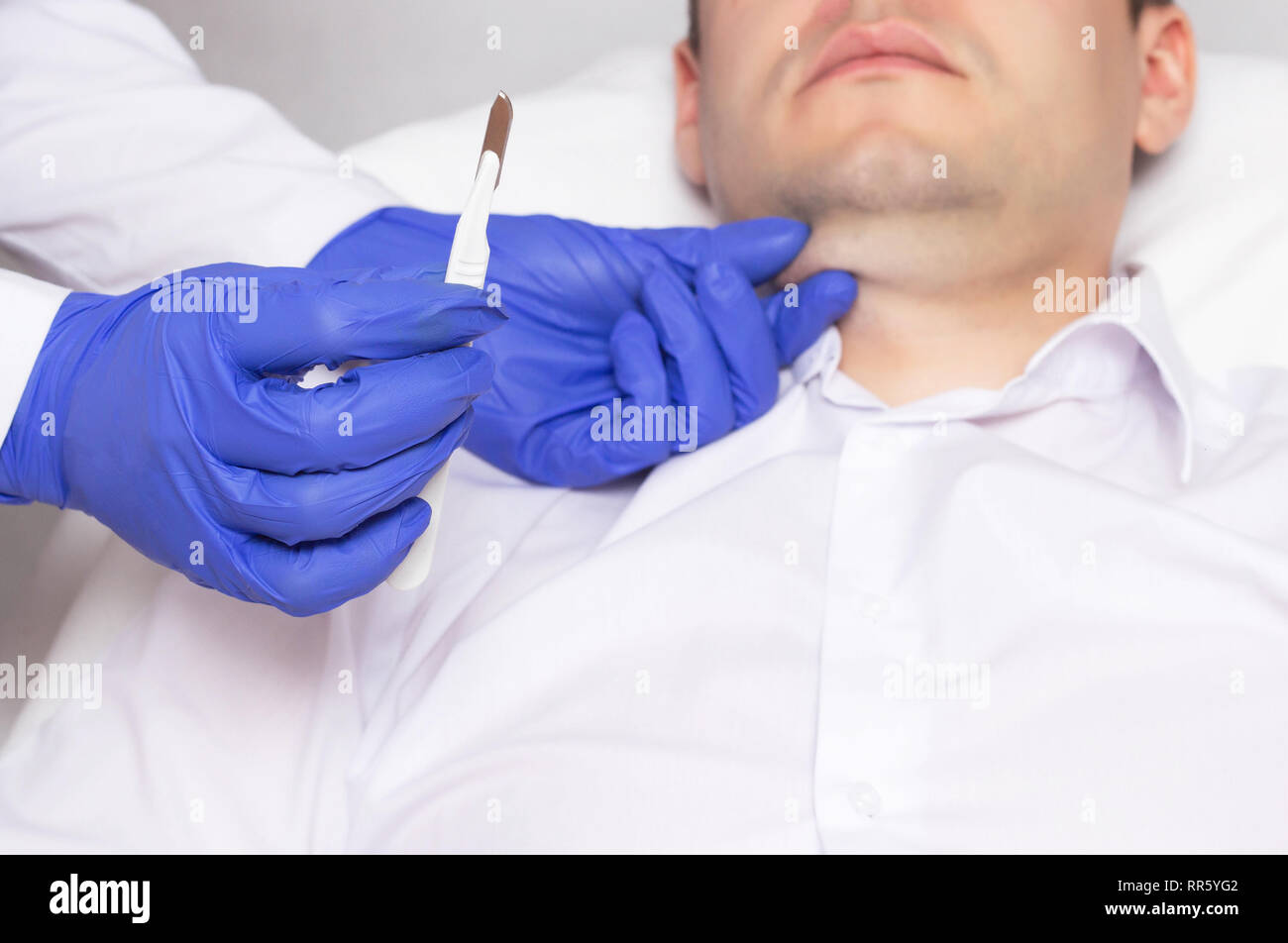 Doctor holding a surgical scalpel on the background of the face of a man with a double chin. Concept of plastic surgery in cosmetology Stock Photo