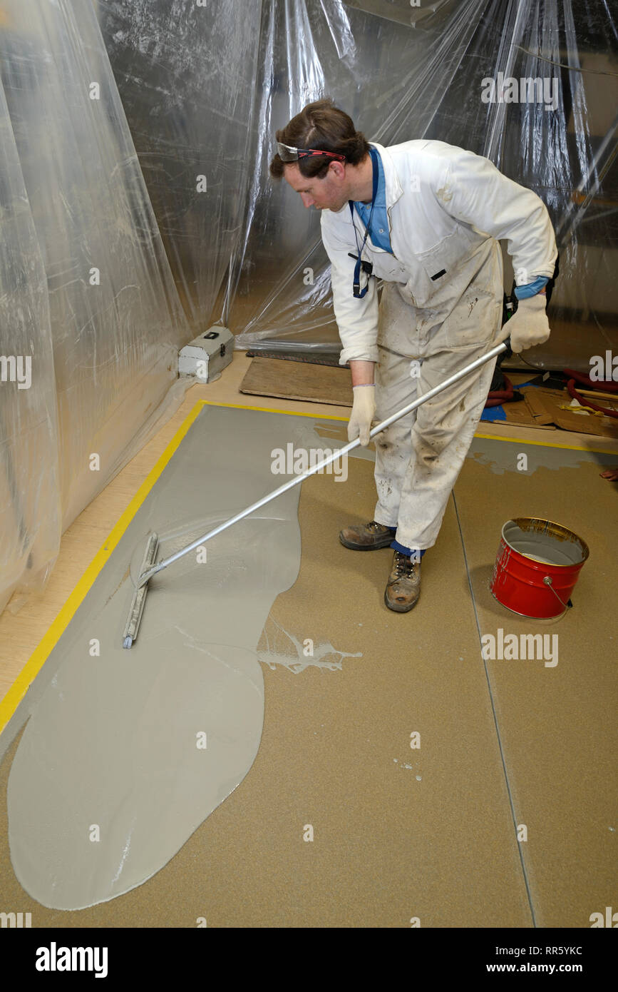 A tradesman spreads an epoxy flooring product in an industrial building. The plastic curtain keeps the job from becoming contaminated. Stock Photo