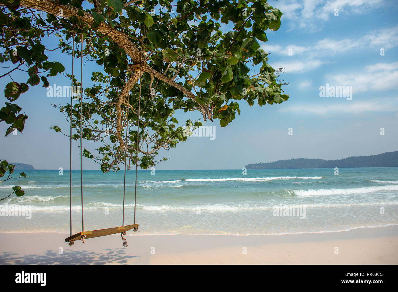 Basic tree hung swing in front of paradise island white sand beach with turquoise sea. Stock Photo