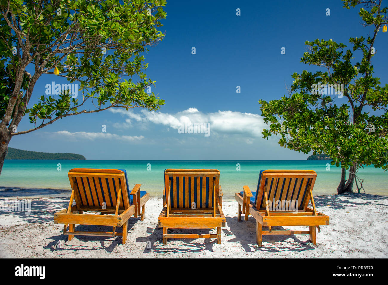 Three luxury wooden sun loungers in a line on a white sand paradise island beach with turquoise sea. Stock Photo
