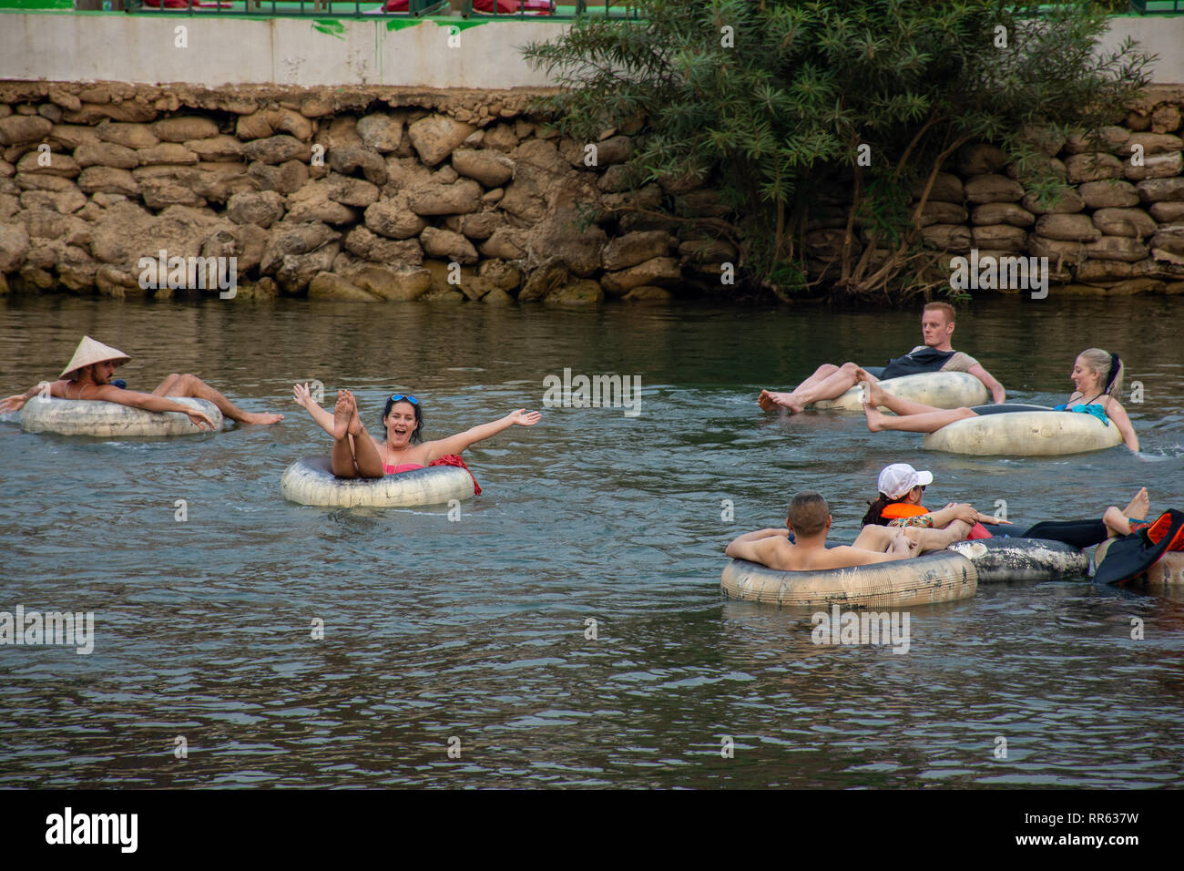 Western tourist back packers enjoy floating and partying in ring tubing, Vang Vieng, Loas. Stock Photo