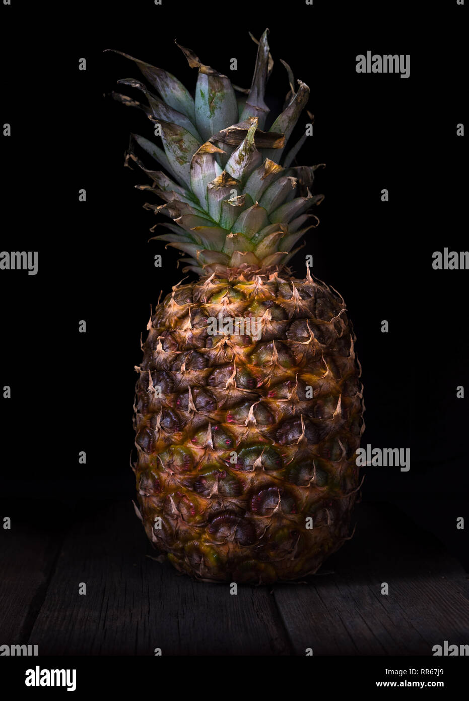 Pineapple on black isolated background on old rustic desk. Stock Photo