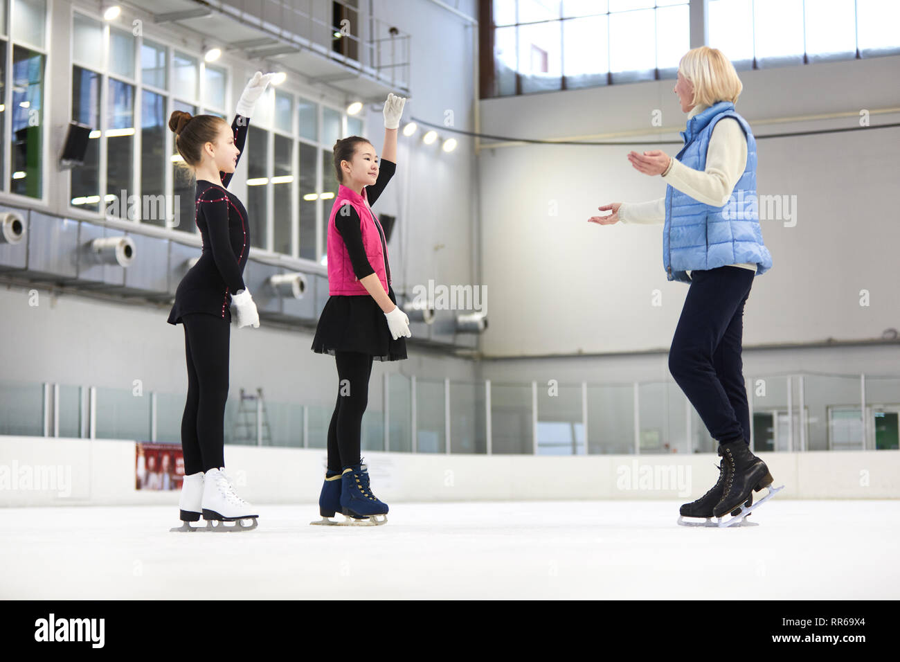 Full length portrait of two girls figure skating on ice rink with